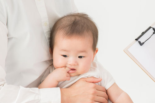 Caregiver holding a baby in a white shirt, baby with fingers in mouth, clipboard visible off to the side